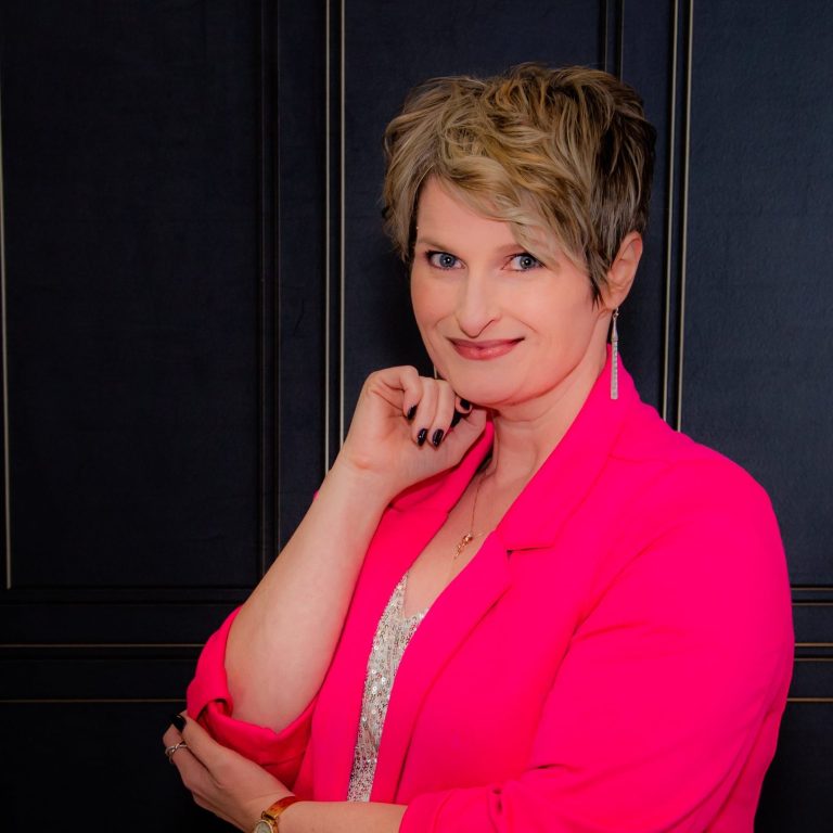 TL Johnson Author of Romantic Suspense in hot pink blazer against dark panel backdrop